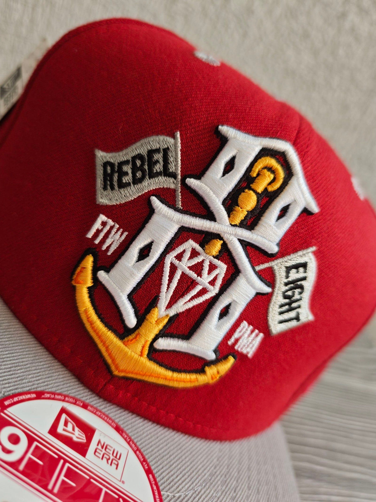 New Era grey and red snapback cap with embroidered "REBEL" anchor design and adjustable strap.