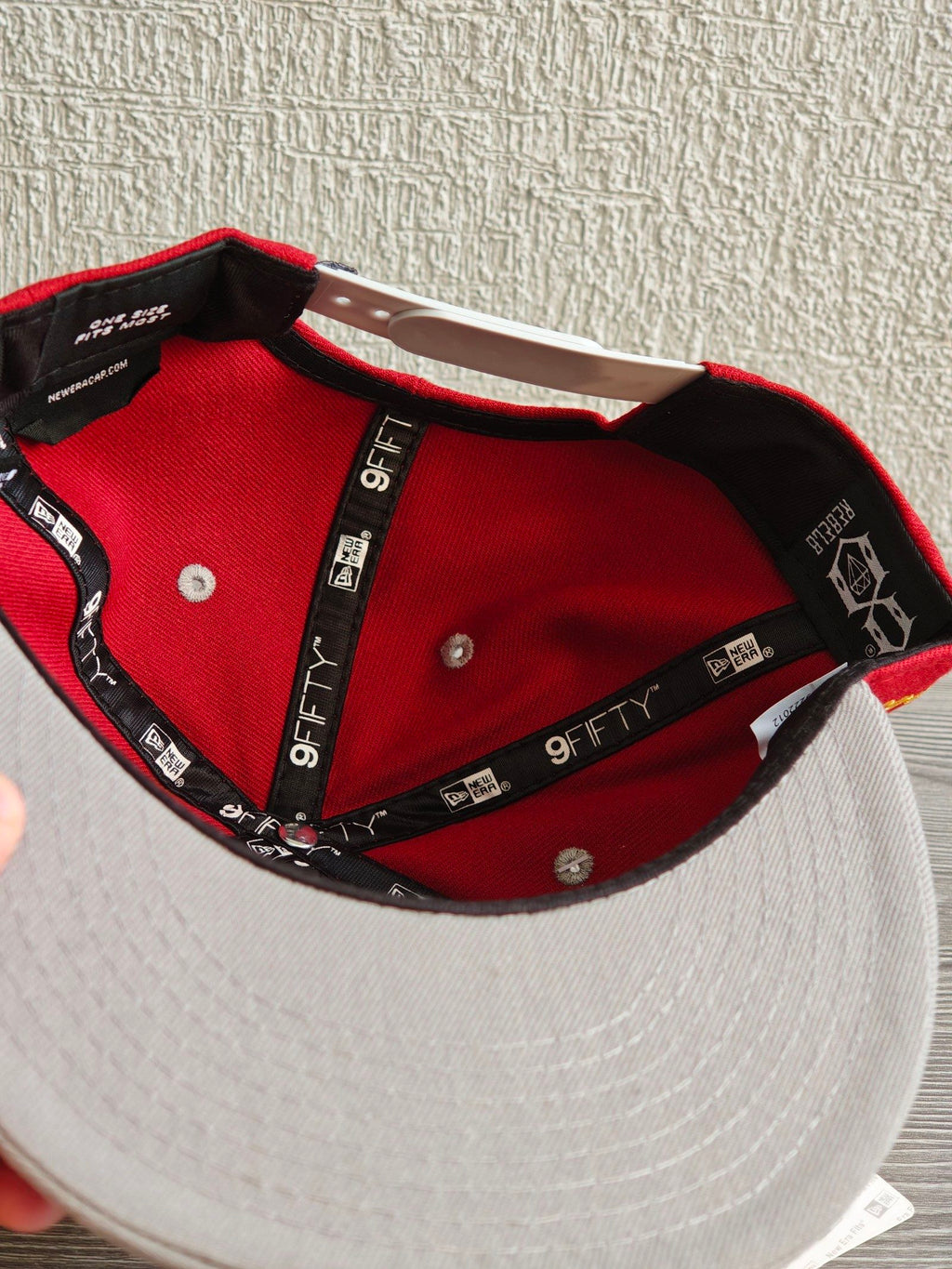 New Era grey and red snapback cap with embroidered "REBEL" anchor design and adjustable strap.