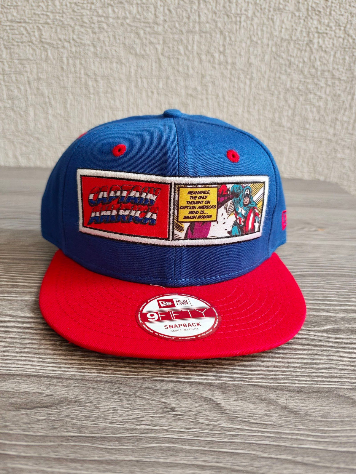 New Era blue and red snapback hat with Captain America comic patch and Marvel logo.