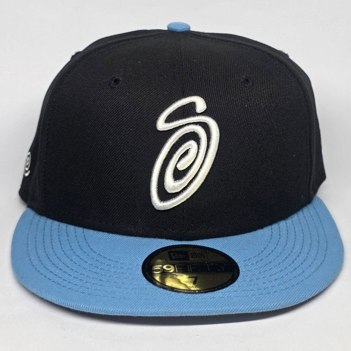 Stüssy black and blue 59FIFTY cap with curly S logo and white detailing.
